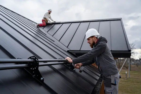 Roofers installing black standing seam steel roofing panels